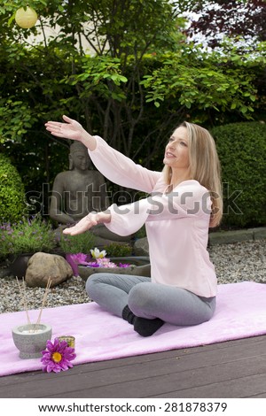 Blond happy middle aged woman with arms outstretched in zen garden