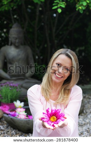 Happy middle aged woman offers flowers in zen garden smiling