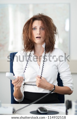Despaired businesswoman sits at her desk with the phone in her hand.