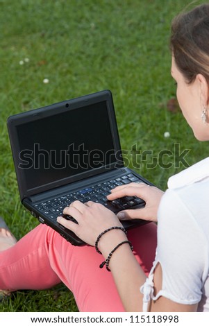 Woman sits on a meadow together with a netbook on her lap