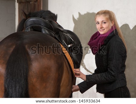 Girl saddles her brown horse (New-Forest-Pony)