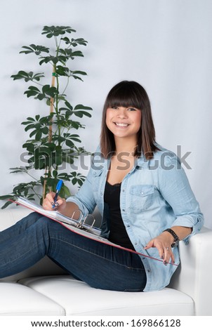 Young, beautiful student sits on the couch and writes into an file.