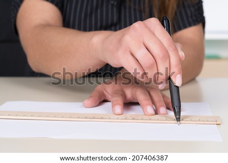 Woman is drawing a line with pen and ruler at the desk.