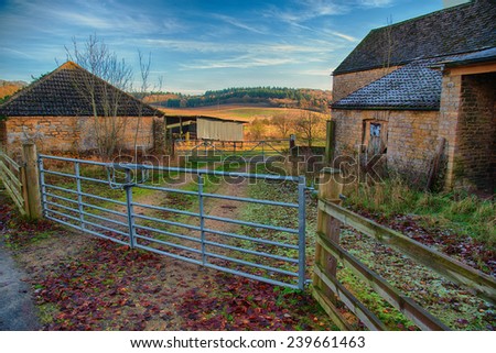 Metal farm gate leading past farm buildings to country side