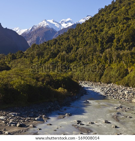 Snowy peak, mountains, forest and clear water in a river. New Zealand. Spring water.