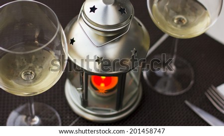 Two glasses of white wine and a metal candlelight with an orange candle. Ready for a romantic dinner. Close up shot.