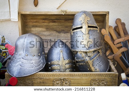 Some handmade old medieval helmets on a wooden box with some other weapons.