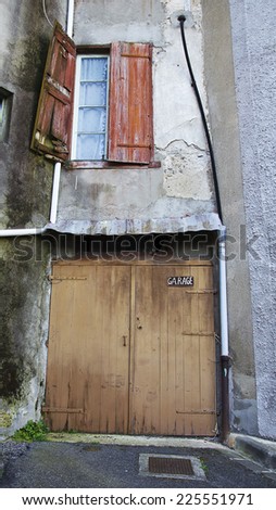 Brown wooden garage door closed. Old thin stone private with a red window building.