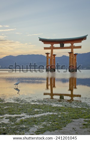 Sunset landscape on a typical Japanese shinto shrine on the Sea shore with sea gulls and quiet water reflection on mountains in the background.
