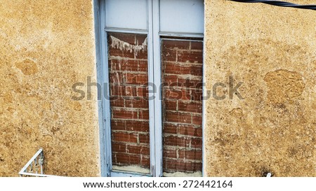 Boarded up brick window on a terrace with blue wood canvas and yellow wall.