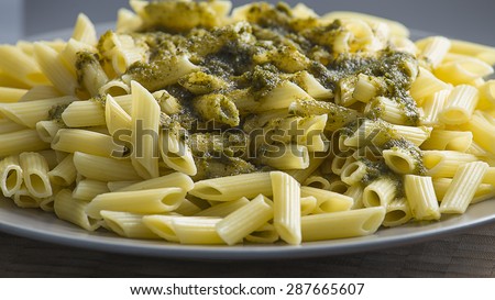 Served Italian green pesto sauce penne pasta close up still in a restaurant. Grey and blue dish with yellow and green pasta.