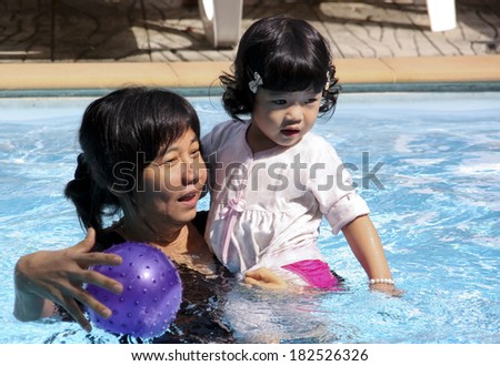 Young girl Child and Grandmother play in swimming pool.Three color balls float in water.Water in pool is glassy.