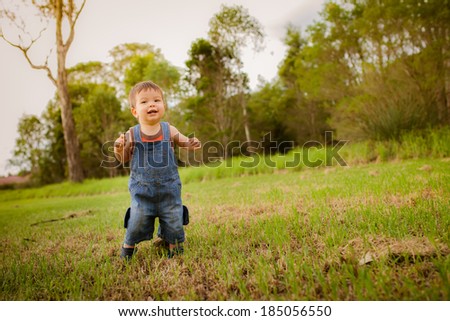 18 month old mixed race asian caucasian boy learning to walk outside in a grassy park on a cool autumn day