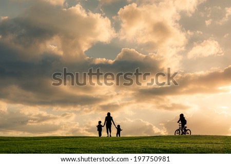 Family silhouette against a bright cloudy sky at sunset. Boy riding a bike with family walking