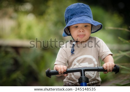 Cute 2 year old mixed race Asian Caucasian boy wearing a blue hat rides his balance bike outside in the summer sun