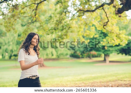 Pretty young brunette woman walking past outside in a park. Filtered effects