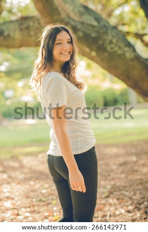 Pretty young caucasian woman wearing black jeans walking outside in a park and turning to look back. Filtered effects
