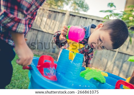 Cute 2 year old mixed race Asian Caucasian brothers play happily with a water toy in their suburban house backyard. Filtered effects