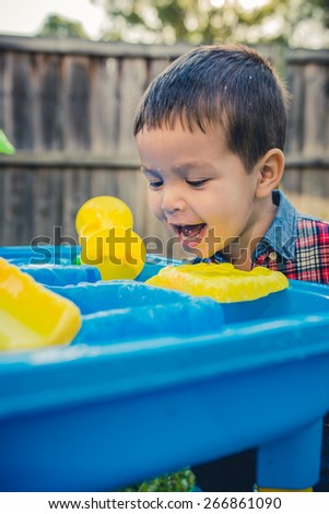 Cute 2 year old mixed race Asian Caucasian boy plays happily with a water toy in his suburban house backyard. Filtered effects