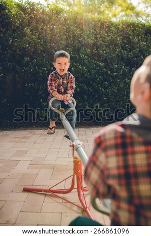 Cute mixed race Asian Caucasian brothers play on a seesaw in the backyard of their suburban home. Filtered effects