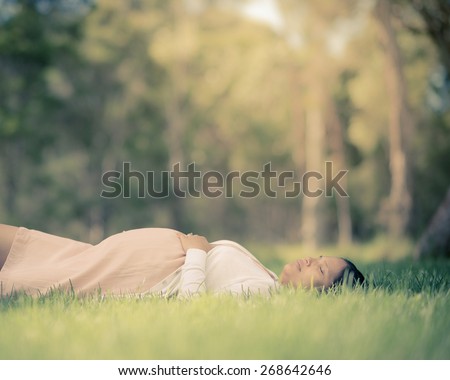 Asian woman 9 months pregnant laying peacefully outside in the grass. Muted tones, faded filtered effects