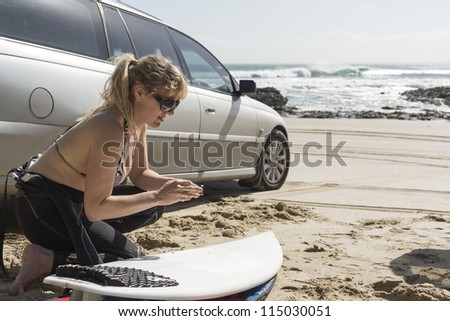 Surfer Waxes Up/ a female surfer prepares her surfboard with great waves breaking in the background