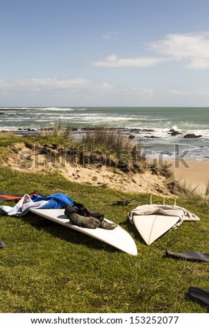 Surfboards/ surfboards and wetsuits laid out in the sun between surfs, with good waves breaking in the background