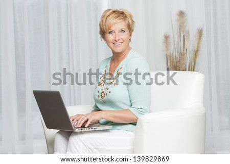 Portrait of a middle aged woman sitting on sofa using laptop and looking to camera