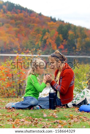 Family picnic: mother and her little daughter drinking hot tea from the thermos in the fall park