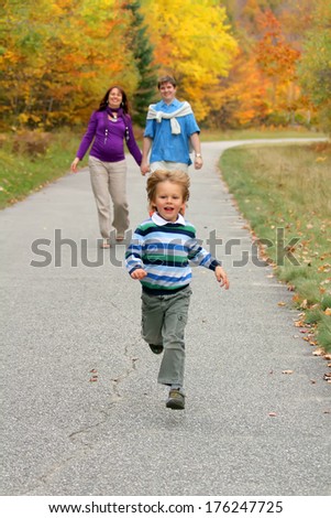 Happy little boy running in the park. His parents watching him from a distance.