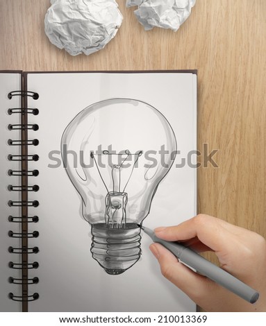 hand with a pen drawing light bulb on note book as concept