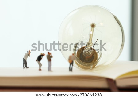 Creative idea concept - miniature photographer with vintage light bulb on open paper notebook