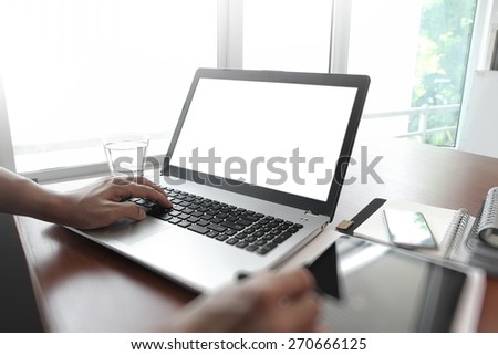 designer hand working with stylus and digital tablet and blank screen laptop on wooden desk in office