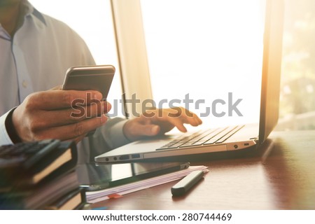 Businessman hand using laptop and mobile phone on wooden desk as concept with overcast effect