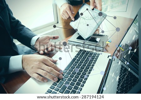 business documents on office table with smart phone and digital tablet and stylus and two colleagues discussing data in the background