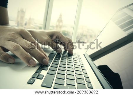 business man hand working on laptop computer on wooden desk with london city blurred background as concept