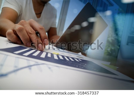 business documents on office table with smart phone and laptop and two colleagues discussing data in the background