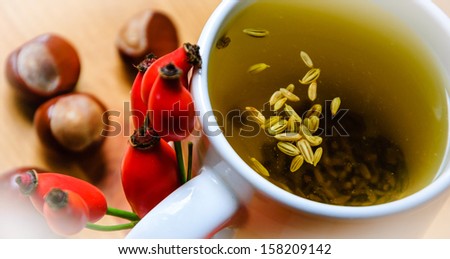 Cup of fennel tea with seeds with rosehip and chestnut decoration. Bleached angles.