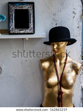 Nude female mannequin with black hat and colorful beads near the entry to the antique store in Paris.