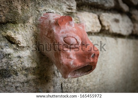 Old ceramic downspout in shape of beast head against stone wall. Closeup. Shadowed angles.
