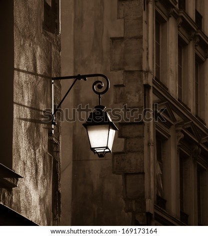 Lantern on the building wall. Paris, France. Sepia. Aged photo. Sunlight is highlighting the lantern attached to the wall and the rest of the street is in the shadow.