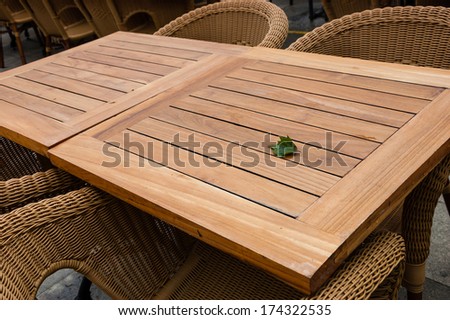 Leaf on the empty table on the terrace of open air cafe. Wooden tables and wicker armchairs.