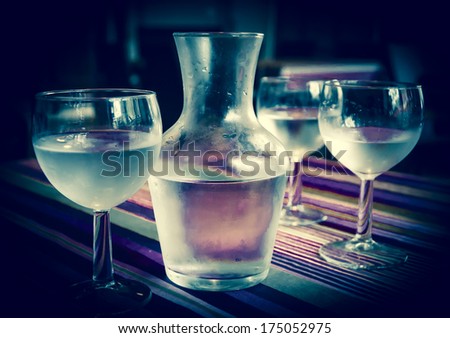 Misted pitcher and three glasses with a water on striped table cloth in french cafe. Reflection, game of light and shadow. Toned image. Selective focus on the pitcher.
