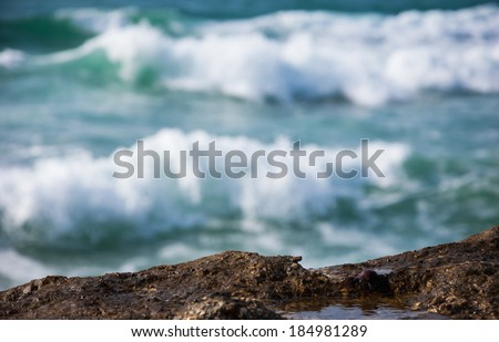 Sea waves with white foam rolling on the rocky coast. Water paddle in the hole. Water wears away the stone concept. Selective focus on the rock.