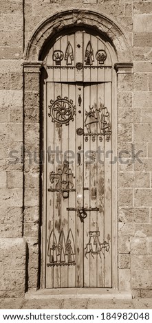 Old wooden door with iron figurative decoration (man travelling on donkey, etc). Architectural detail of Jaffa Clock Tower built in Ottoman period. Jaffa, Israel. Aged photo. Sepia.