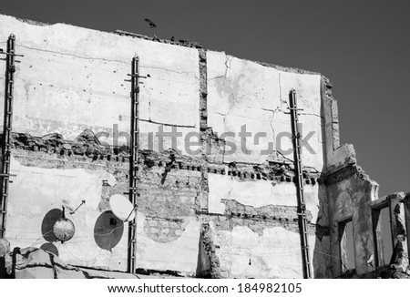 Old ruined house with two rusty satellite dishes and birds (pigeons) sitting over the wall. Nobody.  Life is going on idea. Aged photo. Black and white.