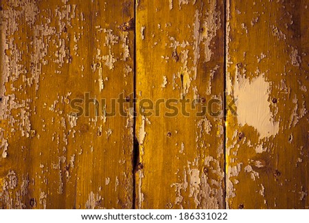 Texture of weathered wooden lining boards with peeling yellow paint and rusty nail heads. Shadowed angles.