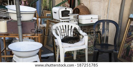 JAFFA, ISRAEL - FEBRUARY 18, 2014: Junk kitchenware and cat, as hostess, sitting on chair at flea market. Jaffa flea market (Shuk Hapishpeshim) is one of tourist main attractions in Jaffa and Tel Aviv