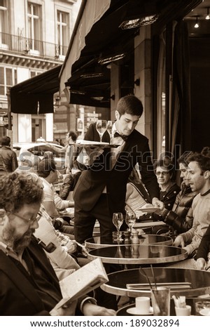 PARIS, FRANCE - APRIL 20, 2014 : Waiter serving customers at traditional outdoor Parisian cafe in center city.
