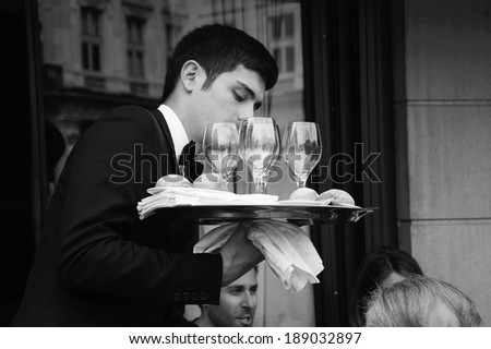 PARIS, FRANCE - APRIL 20, 2014 : Waiter serving customers at traditional outdoor Parisian cafe in center city. Street buildings are reflected in the glasses.